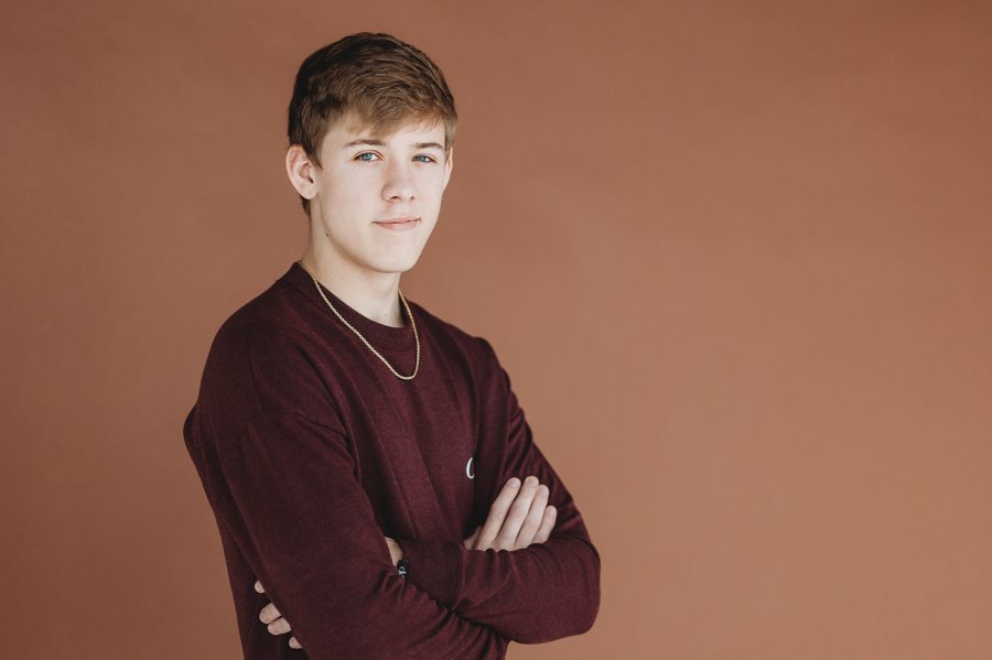 Grove City Senior Pictures of Alex on a rust background wearing maroon sweater with arms crossed