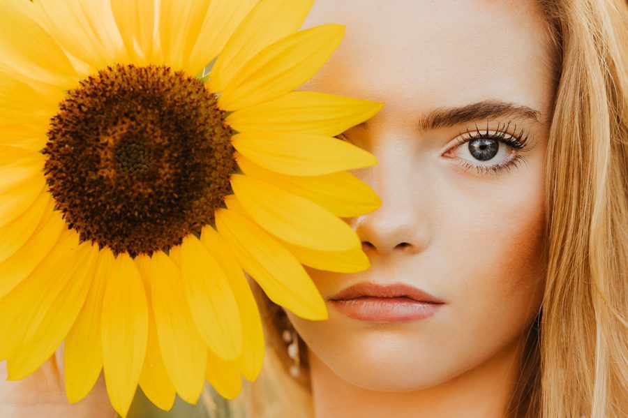 Grove City Senior Photographer Carmilla Jane captures Darby posing with a sunflower over one of her eyes.